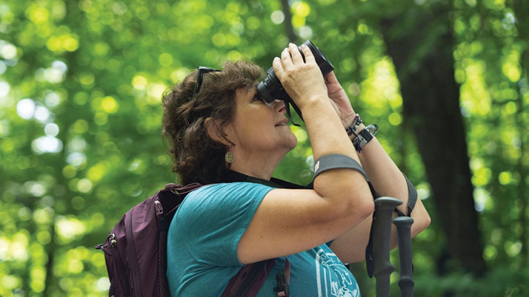 woman in forest looking with binoculars