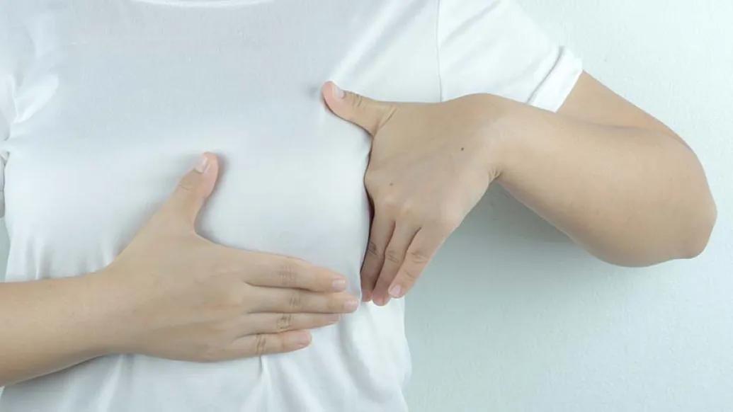 person doing self breast exam over white shirt