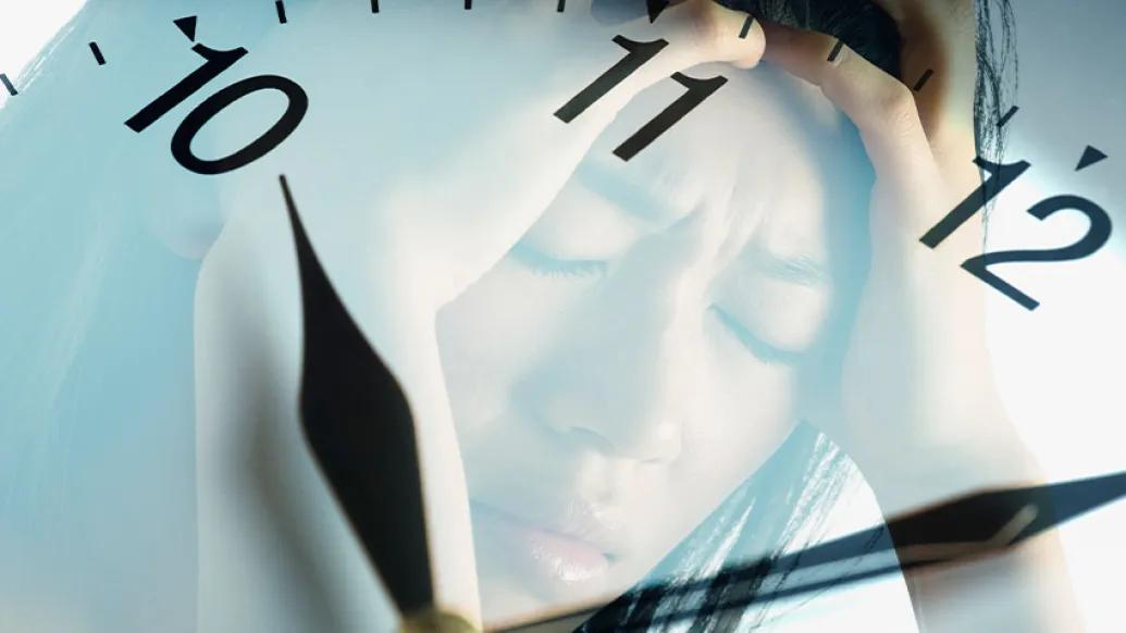 woman reflected in clock holding head in pain