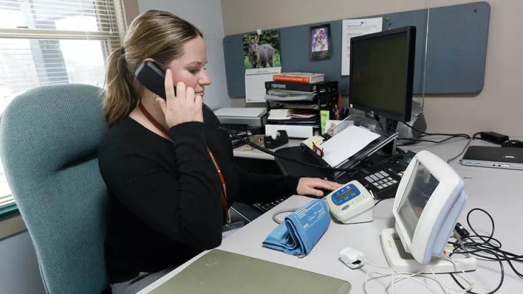 woman sitting at desk wearing black shirt and on phone while reading blood pressure