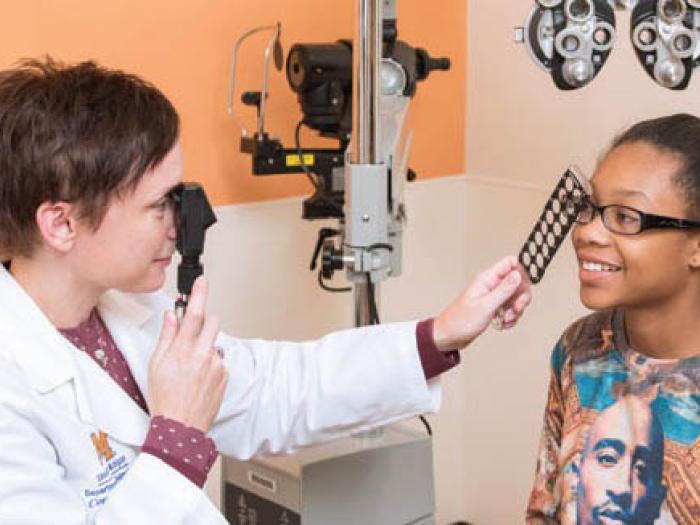 White female eye doctor examining young Black girl's eyes