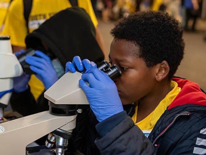 Black boy wearing blue surgical gloves looking into microscope