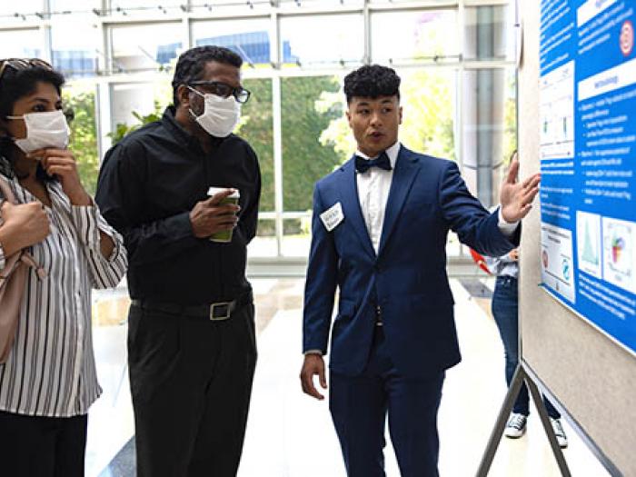 Black student in suit and bowtie presenting poster