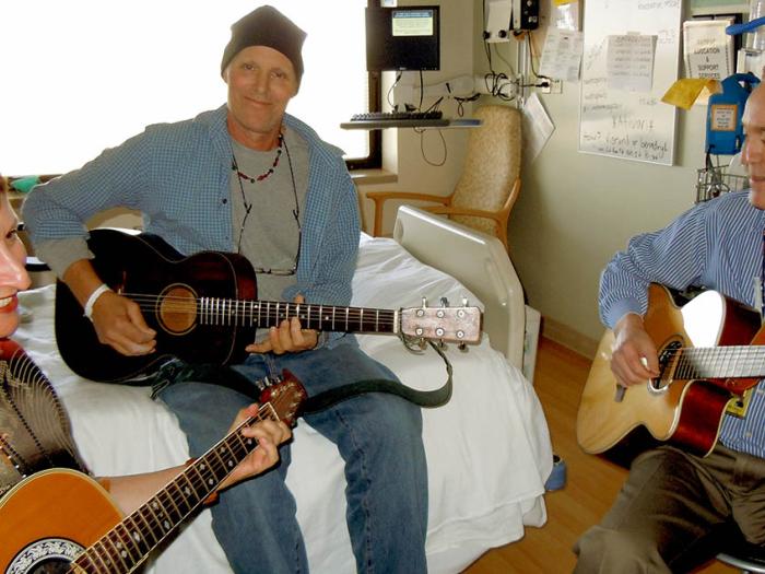 Two men and one woman playing guitar in hospital room