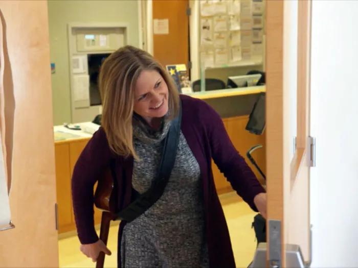Woman with guitar smiling while peeking around the corner of a patient room