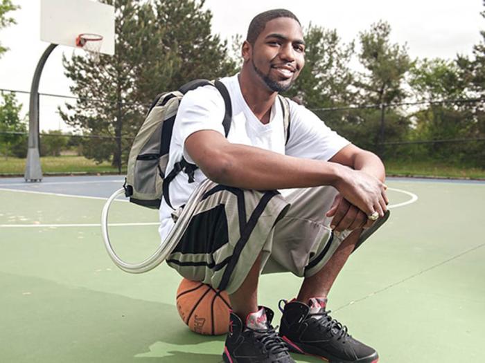 Young black man with medical backpack sitting on basketball on basketball court