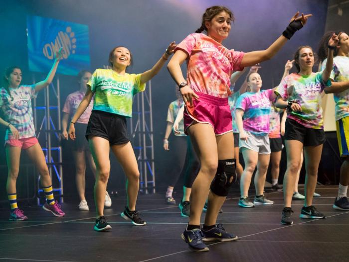 group of dance marathon students wearing bright colored shorts and t-shirts dancing on a stage