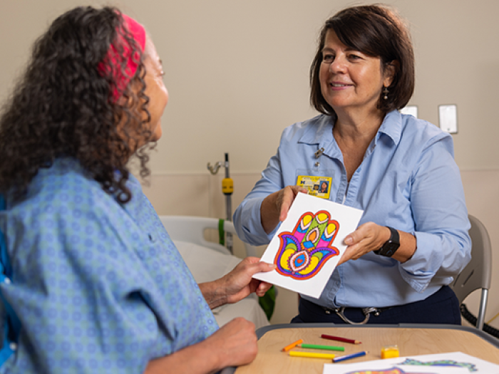 female staff member and patient holding a hamsa art page