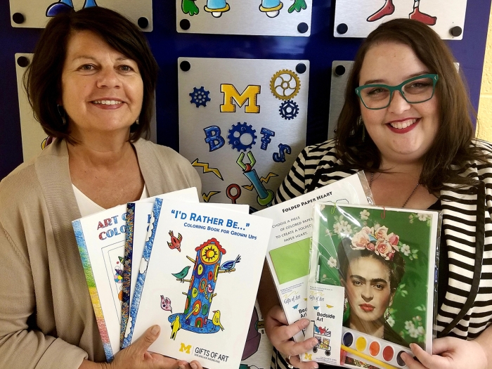 Two women smiling and holding coloring books and art projects