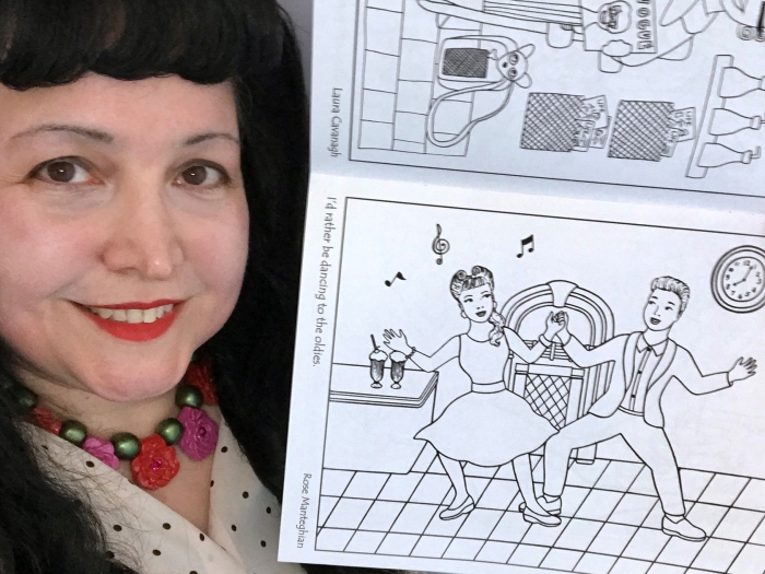 Dark-haired woman with flower in hair and red lipstick holding up coloring book with dancers to color