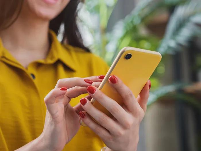 woman with red nail polish wearing a gold shirt holding an mobile phone
