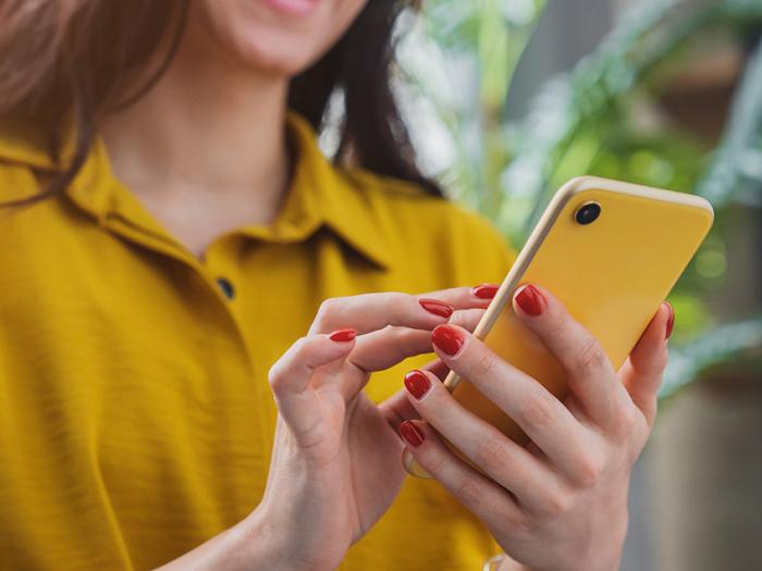 woman with red nail polish wearing a gold shirt holding an mobile phone