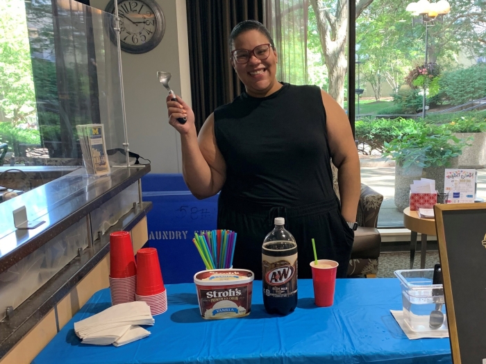 Woman smiling and holding up spoon with root beer and ice cream on table in front of her