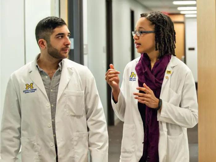 Two medical students, one male and one female, talking while walking down a hallway