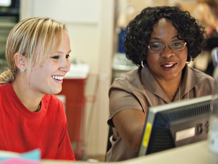 Black woman and white woman seated in front of computer smiling