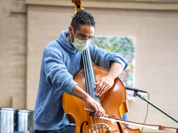 Black man wearing blue turtleneck playing string bass with art in background