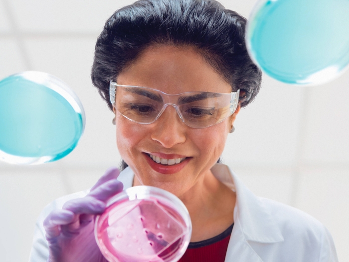 Female scientist wearing goggles looking at petri dishes on a glass table