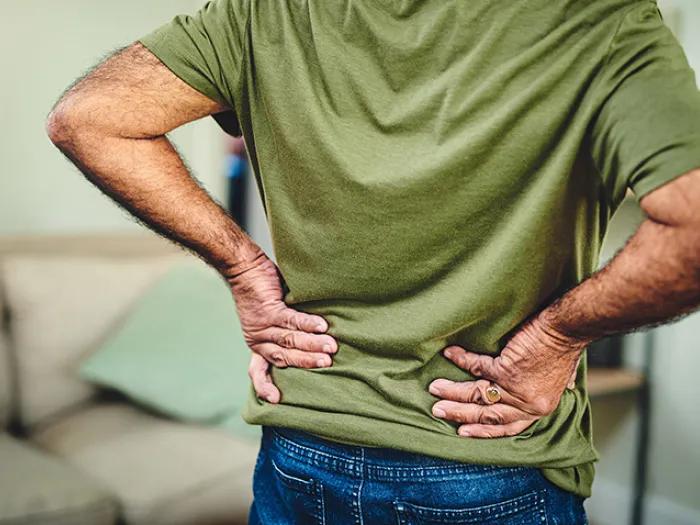 The back of a man in a green shirt with his hands on his lower back