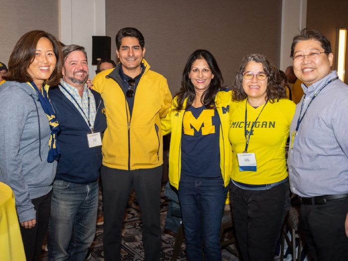 A group of 6 Medical School alumni wearing University of Michigan gear, pose together.