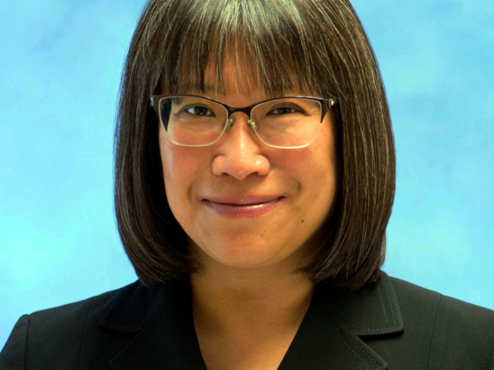 Professional portrait of a middle aged Asian woman who has shoulder-length black hair and is wearing glasses and a black blazer