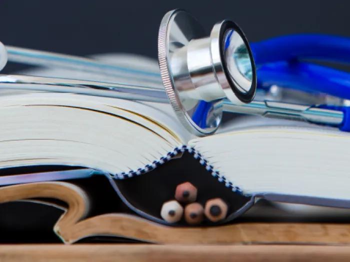 Close up image of an open book with a blue stethoscope resting on it. 