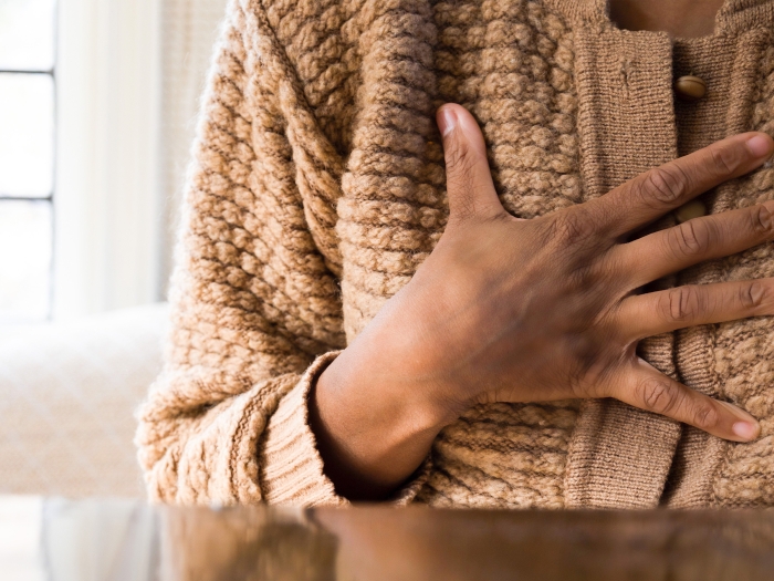 Woman holding her hand on chest wearing tan sweater