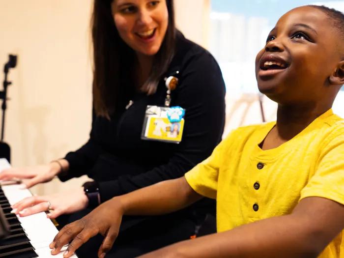 yellow shirt kid looking up very happy wearing playing piano with employee with white shirt 