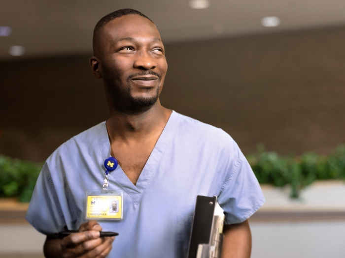 Black man with mustache and trimmed beard wearing blue scrubs and U-M name badge