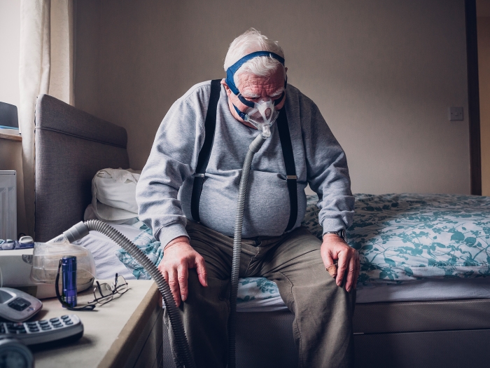 older man on cpap machine sitting on bed