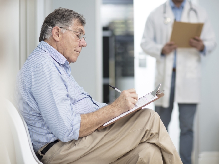 older man sitting filling out form in doctor's office