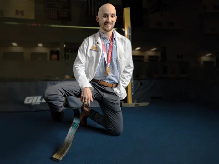 Man kneeling, wearing a doctor's white coat. His right leg has a prosthetic. 