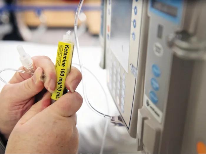 Close-up of a nurse's hands holding a syringe of ketamine that she is attaching to IV tubing