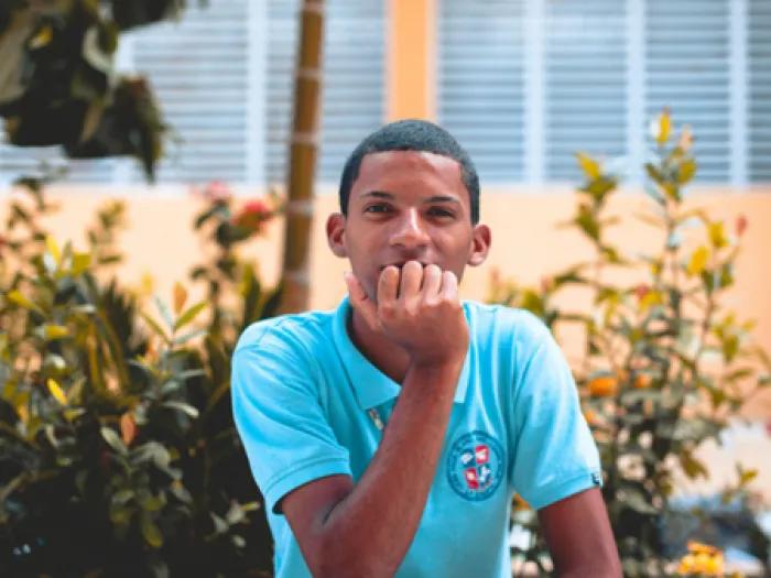 Stock image of a young person outside surrounded by foliage. They are wearing a bright blue polo. 