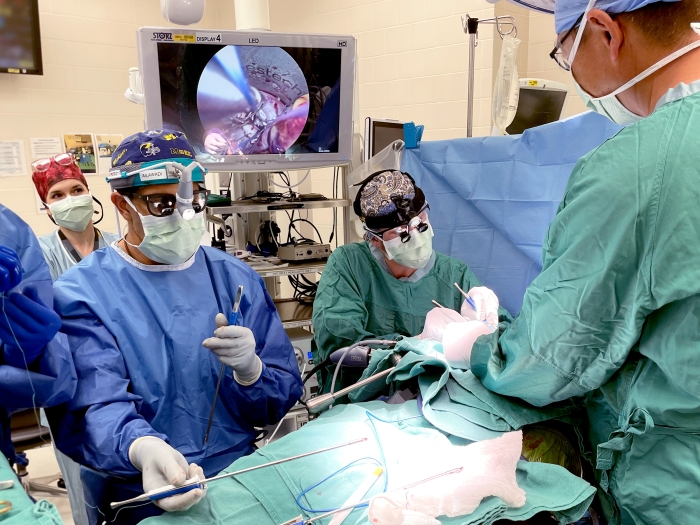 surgeons in OR with blue and teal scrubs with screen on and patient under teal sheet