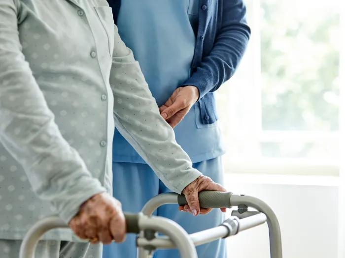 person holding walker with nurse next to them closer up on hands lower body