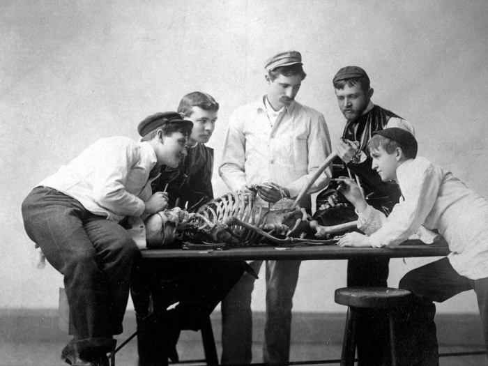black and white photo from the 1800s of medical students examining a skeleton