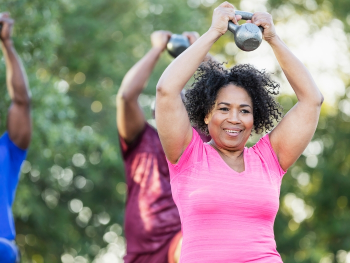 Woman in pink shirt lifts kettleball in an outdoor exercise class