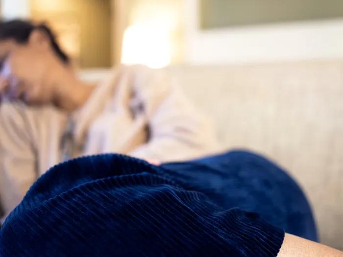 Woman sleeping on a couch holds her stomach, as if in pain