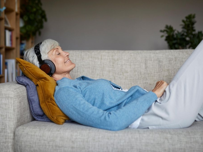Older woman listening to music with headphones as she lays on a couch.
