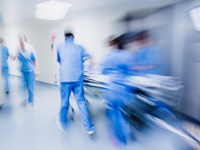 Blurred image of health care professionals in blue scrubs pushing a gurney down a hallway