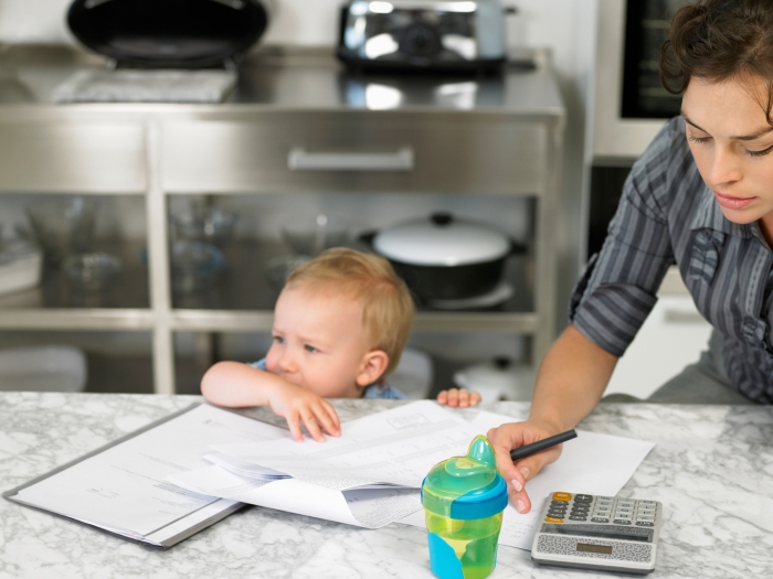 Mom at table with baby, working on calculator with stressed out first expression