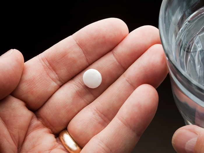Person's hand holding an aspirin tablet with a glass of water nearby