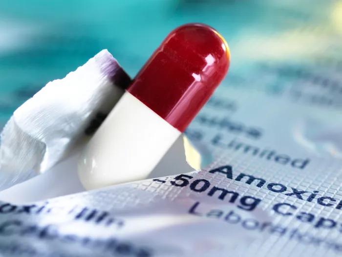 Pill capsule pushing through a paper with amoxicillin printed on it.
