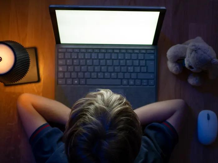 child on comp screen dark room with teddy bar blonde hair