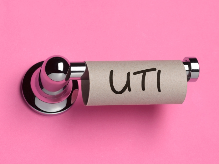 uti written on empty roll of toliet paper on a toliet paper holder with hot pink background