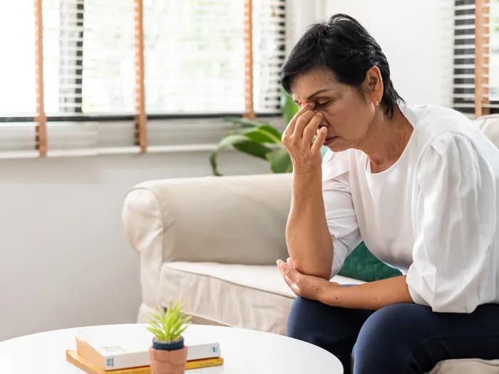 woman holding face looking stressed on white couch in white shirt dark blue pants