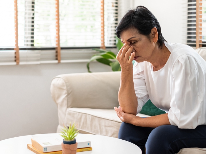 woman holding face looking stressed on white couch in white shirt dark blue pants