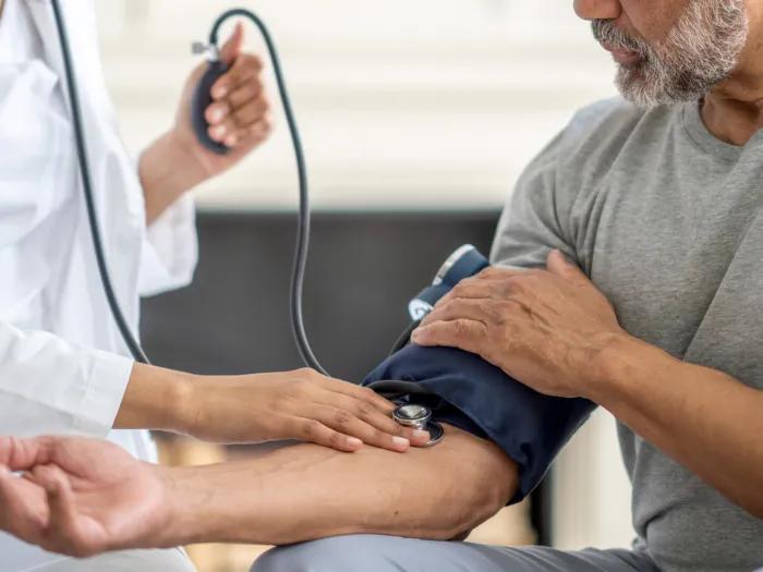 blood pressure cuff on mans arm with white coat doctor taking it 