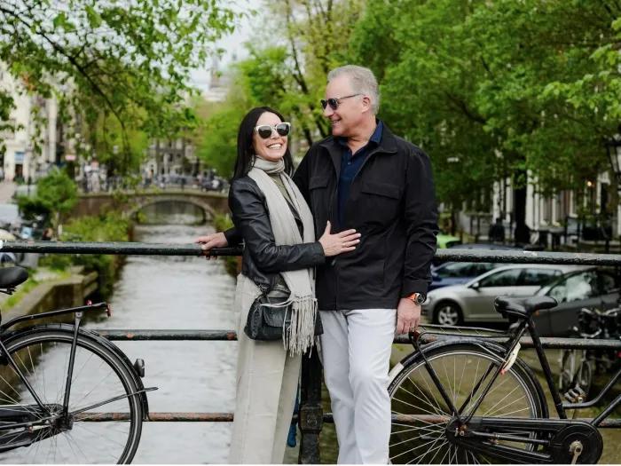 Smiling portrait of the Eisenshtadts standing together on a small bridge over a tree-lined urban canal.