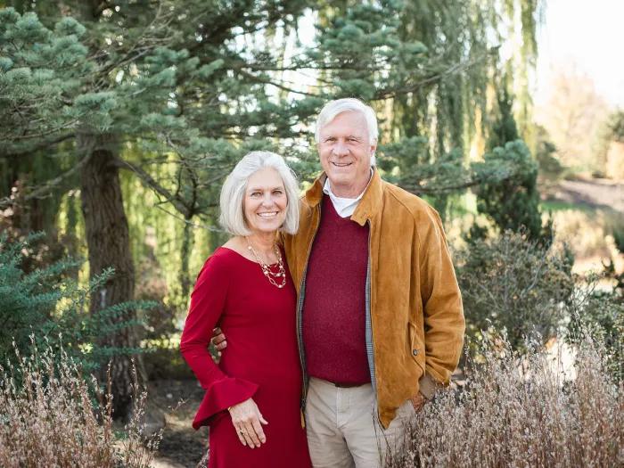 Smiling portrait of Bob and Patti Huiskamp standing together with a beautiful nature scene in the background.